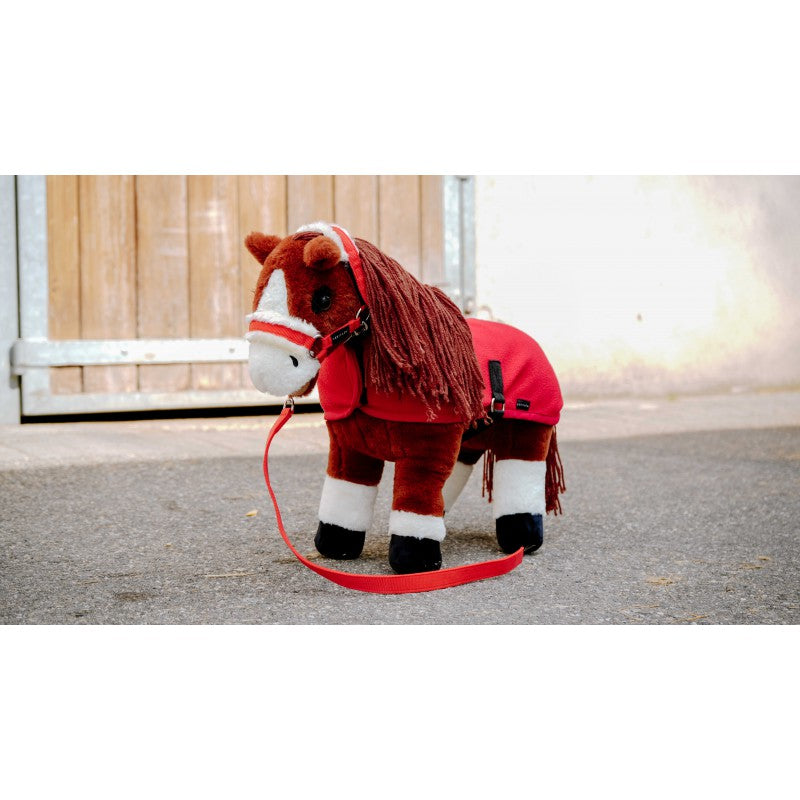 Plush toy horse with a red blanket and reins on a leash, standing on a concrete surface.