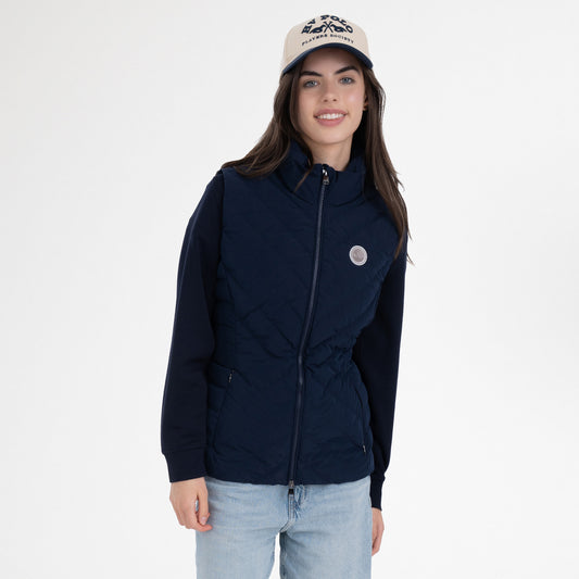 Girl wearing a navy gilet, navy hoodie, navy and beige cap and blue jeans on a white background