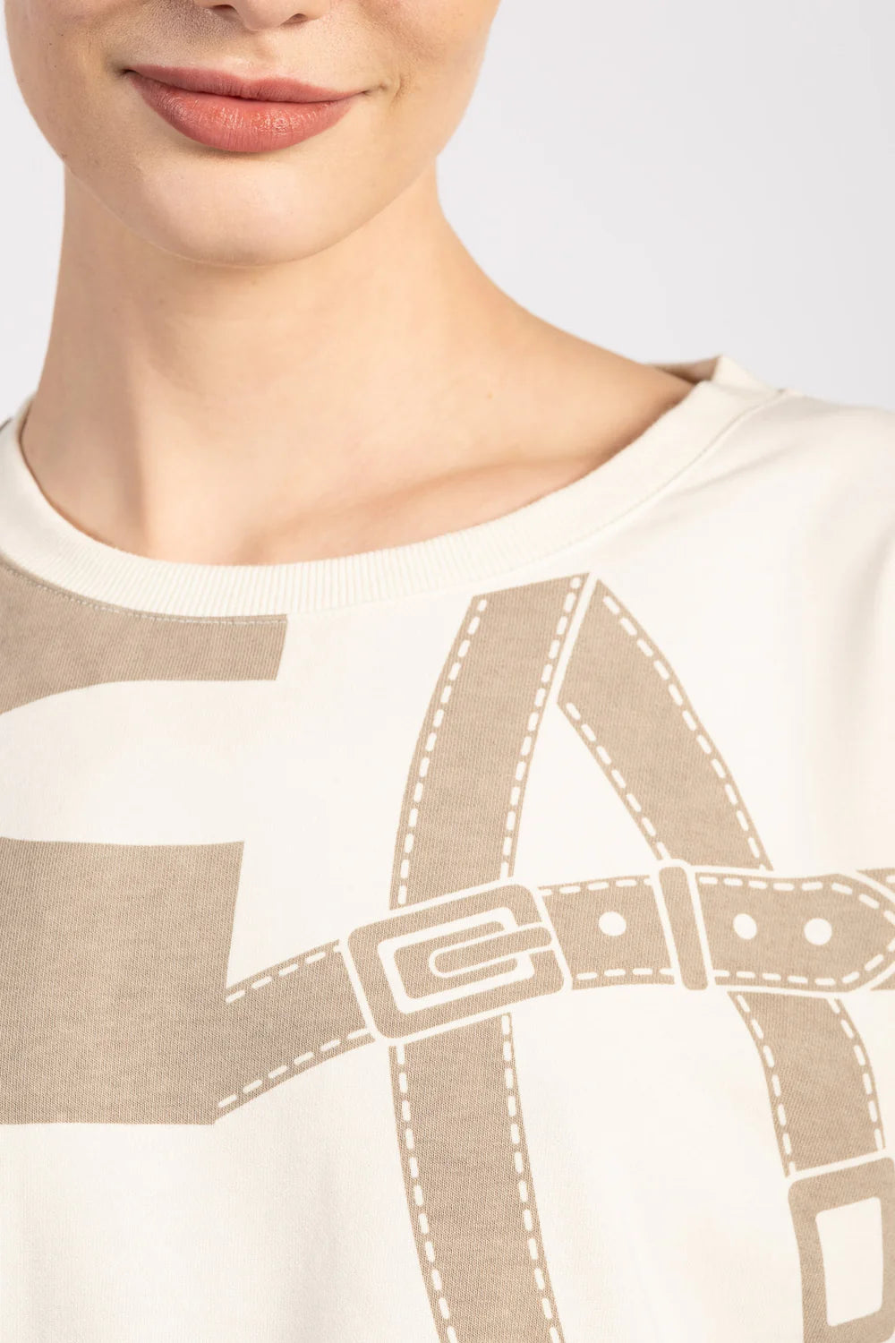Woman wearing a beige sweater with equestrian motif on a white background