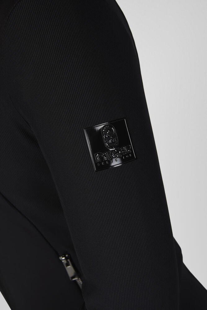Close-up of a black ribbed knit garment sleeve featuring a glossy black rectangular Stone Island logo patch on the upper arm.