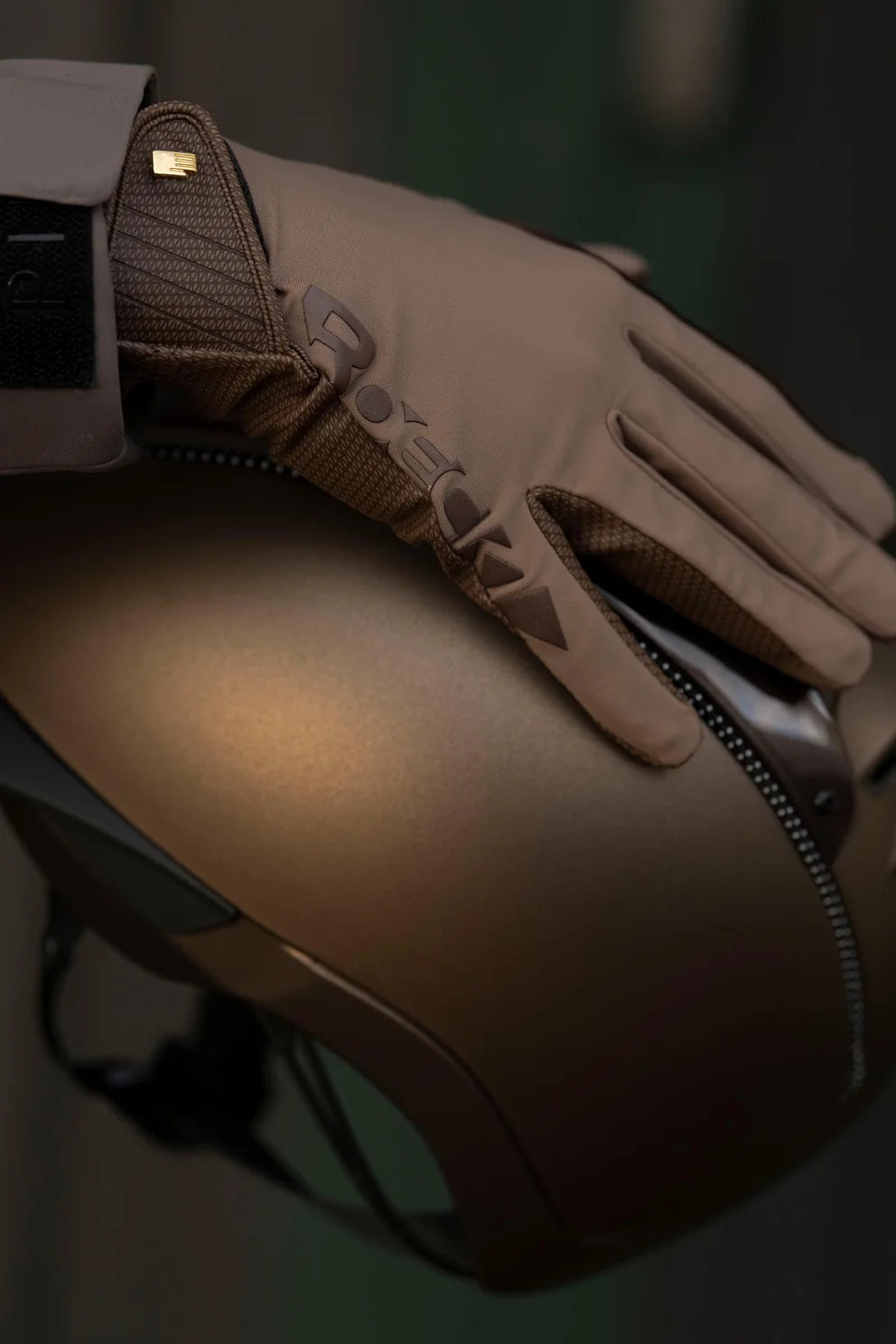 A close-up of a tan leather riding glove with a zipper and textured knit cuff, resting on a matching tan motorcycle helmet.