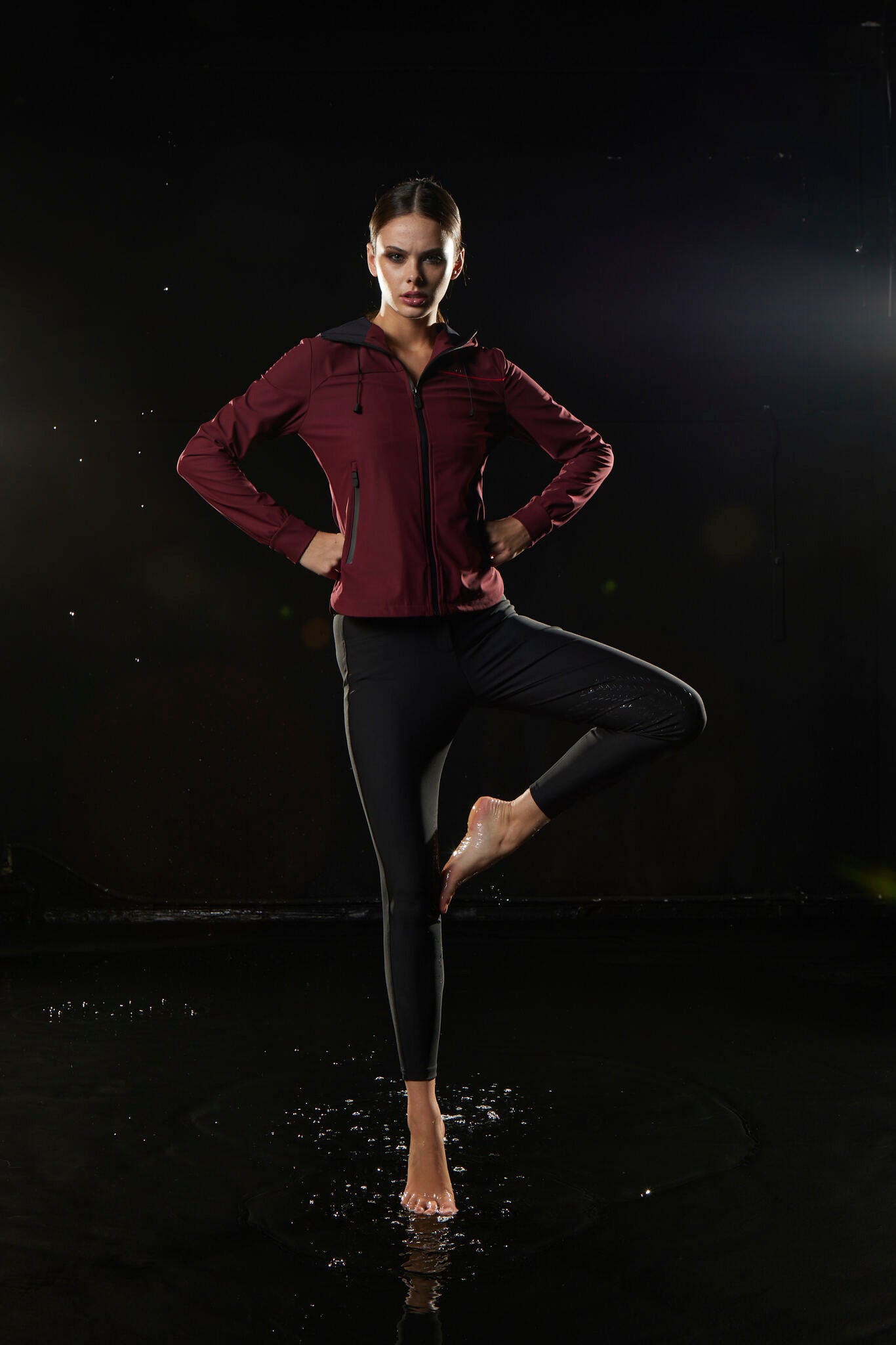 Person wearing a maroon jacket and black leggings on a dark background