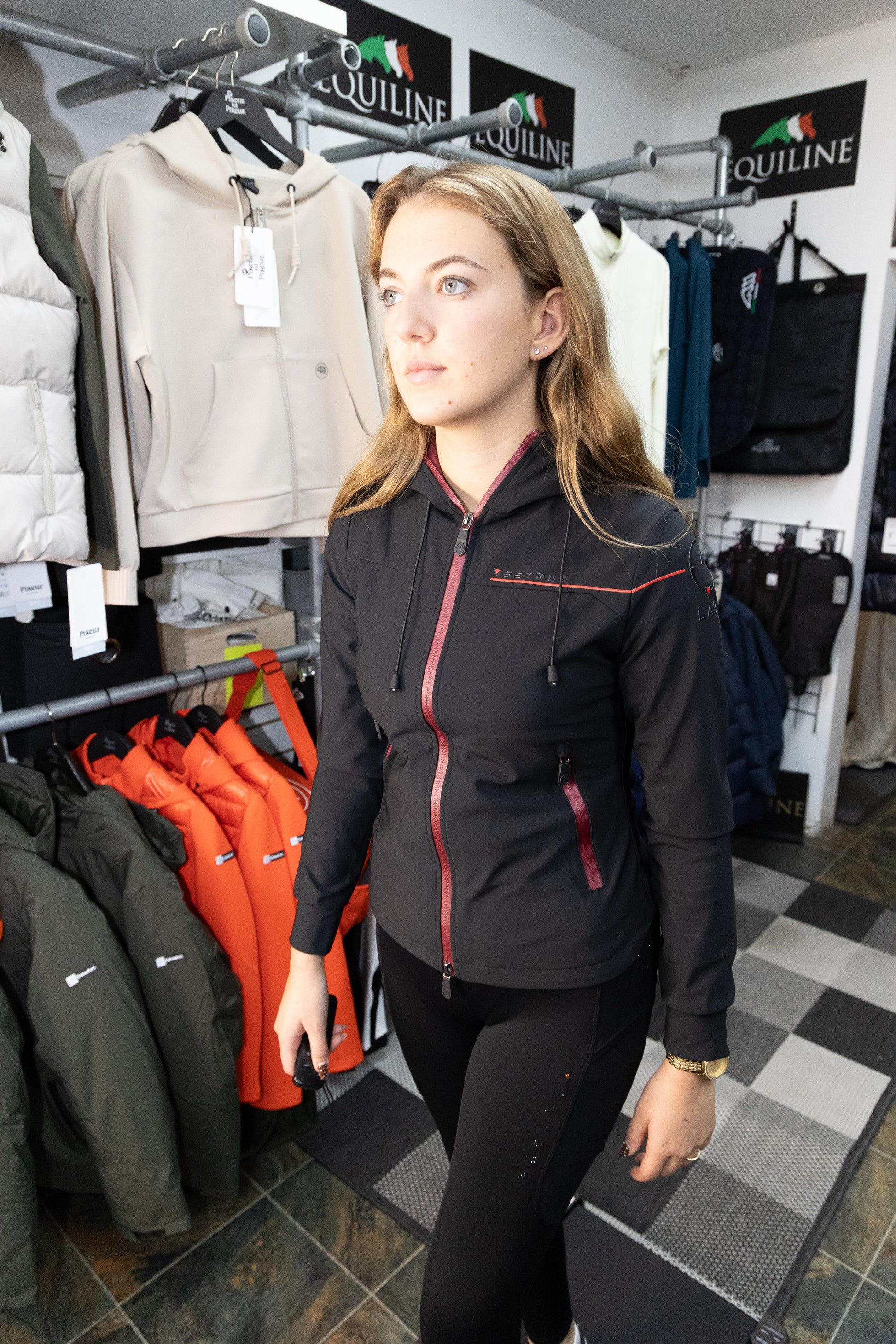 Woman wearing a black jacket in a store with outdoor gear on racks