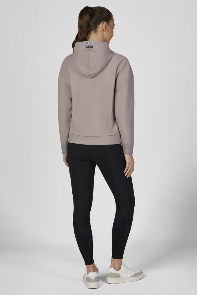A woman shown from the back wearing a light taupe-pink hooded sweatshirt and black leggings, standing against a light gray studio background.