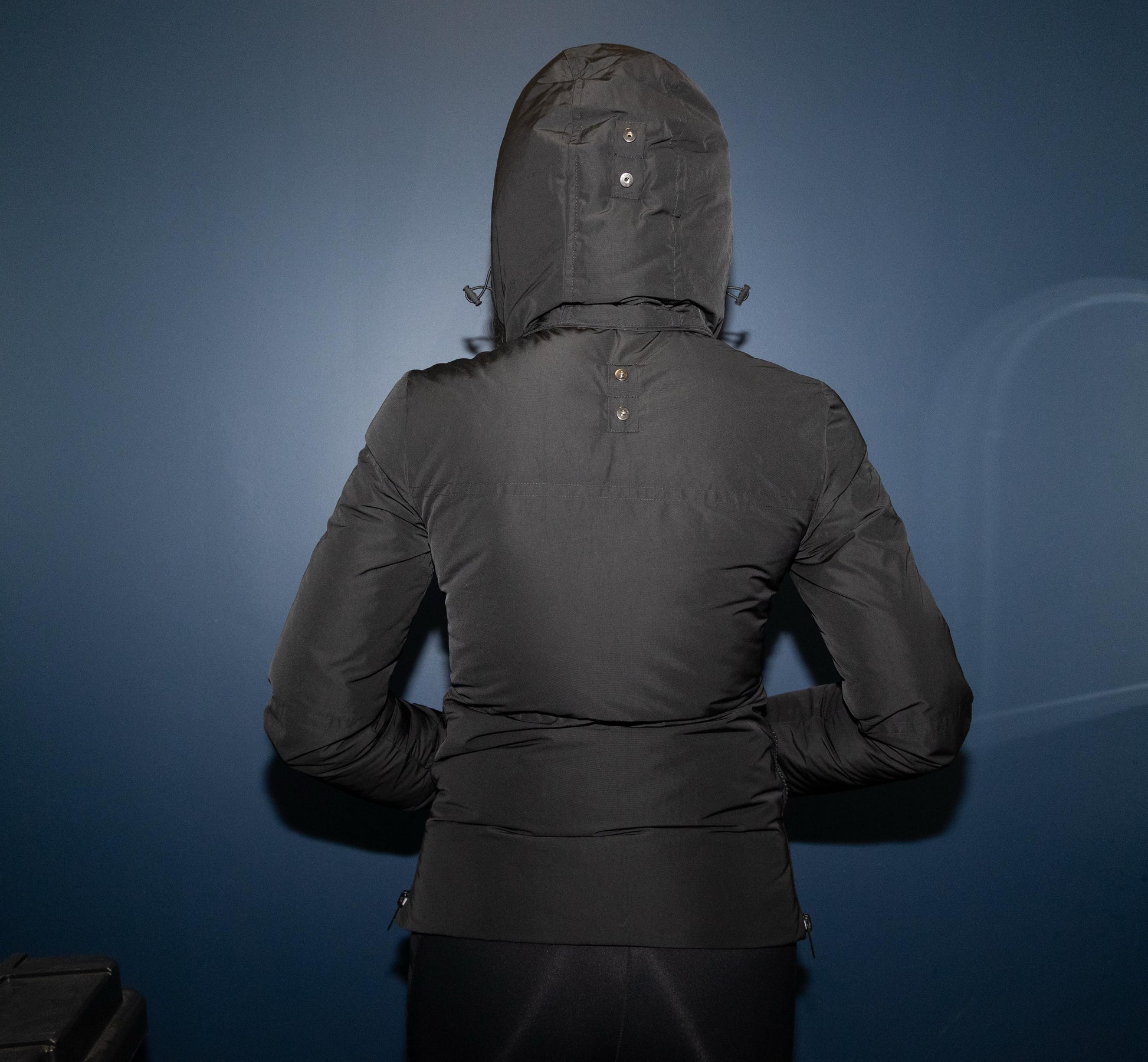 Person wearing a black hooded jacket against a blue background