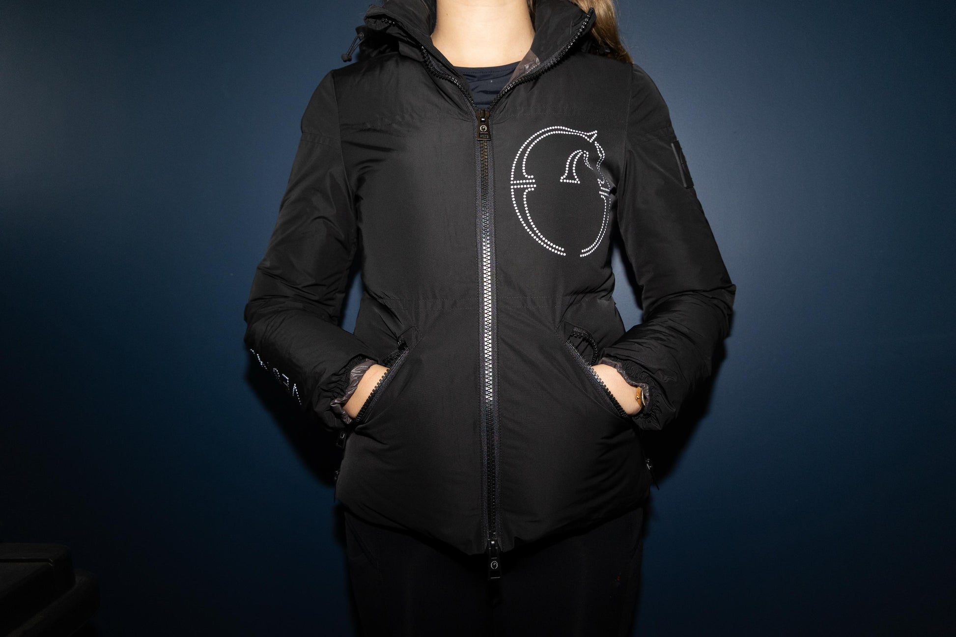 Person wearing a black jacket with a logo on a dark background