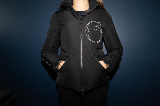 Person wearing a black jacket with a logo on a dark background