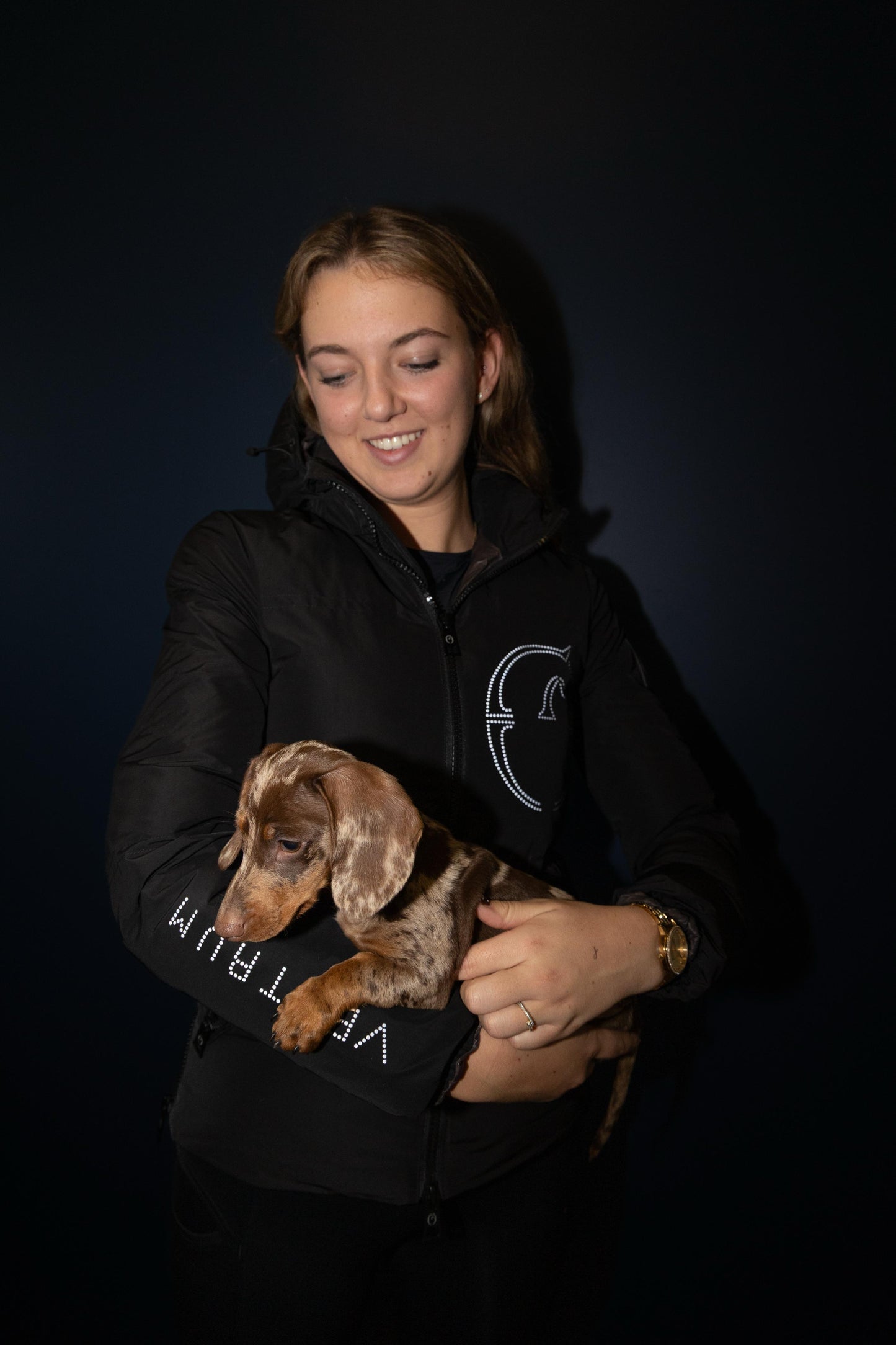 Person holding a small dog against a black background