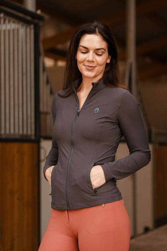 Woman wearing a dark gray jacket and pink leggings standing in an indoor setting.