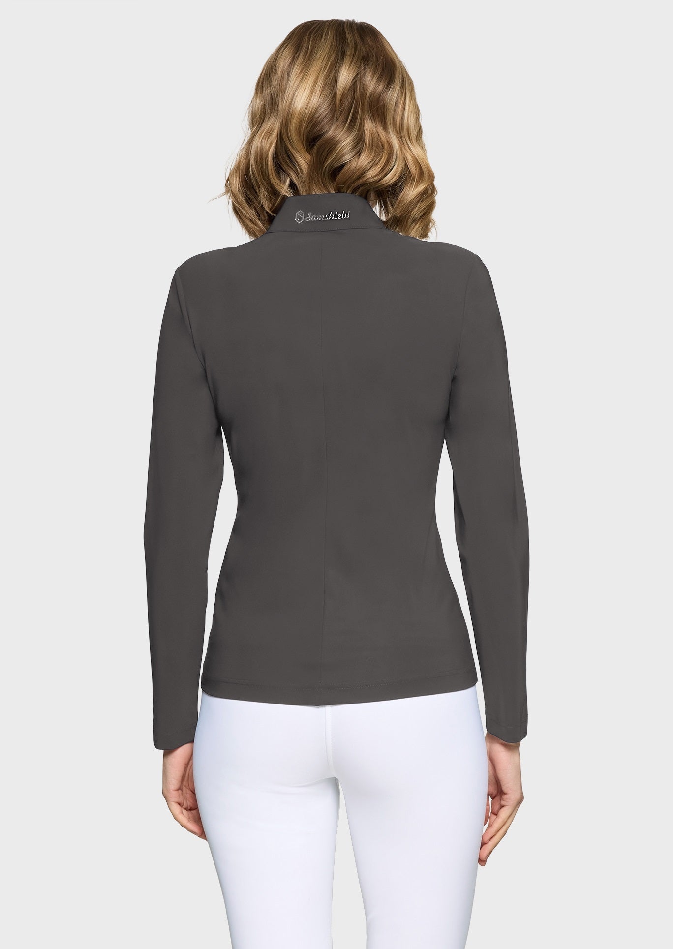 Woman wearing a grey full zip training top and white breeches on a beige background