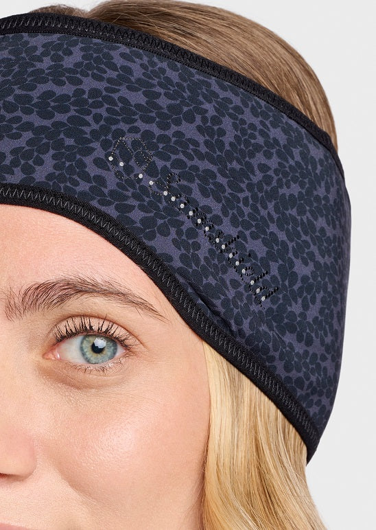 Close-up of a woman wearing a dark navy blue athletic headband with a black floral pattern and rhinestone embellishments. The headband is shown on a model with blonde hair and blue eyes against a light gray background.