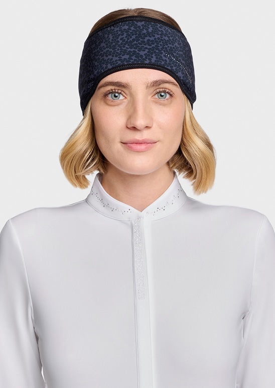 A woman with short blonde hair wearing a dark navy patterned headband and a white high-neck top, shown against a light gray studio background.