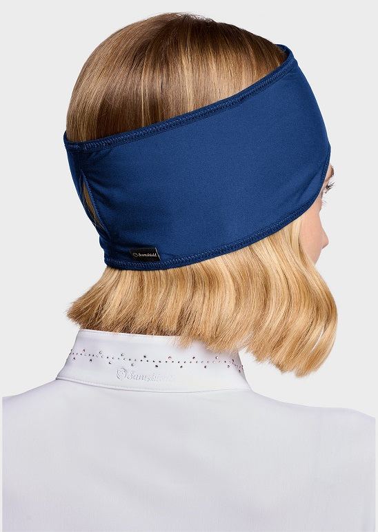 A woman shown from the back wearing a navy blue athletic headband, with blonde hair and a white collared shirt visible against a light gray studio background.