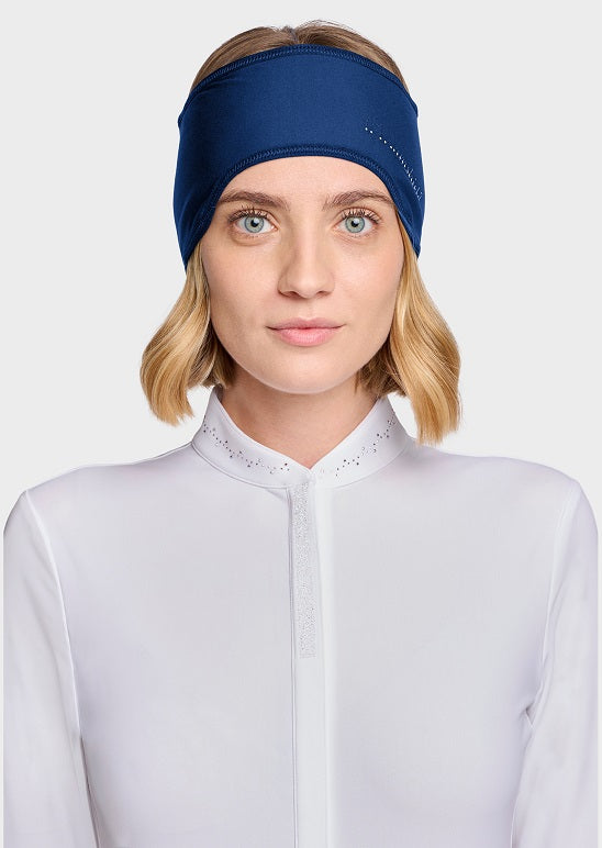 A woman with blonde hair wearing a navy blue athletic headband and a white high-neck athletic top, photographed against a light gray studio background.