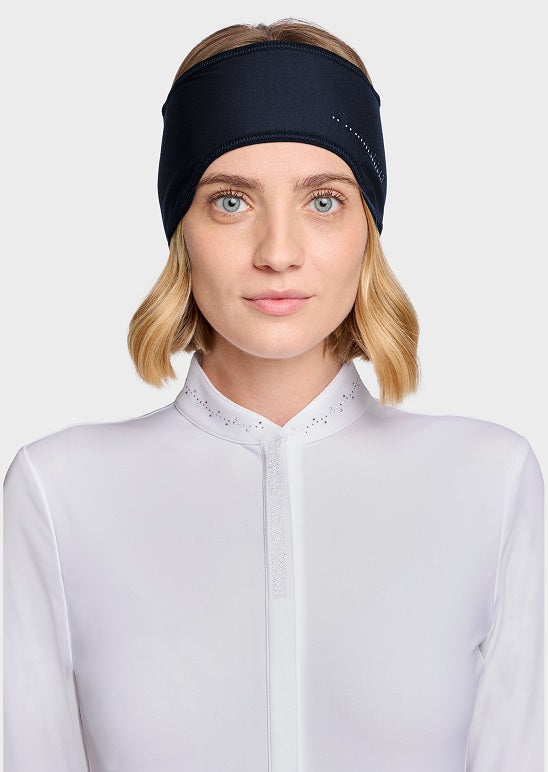 A woman with blonde hair wearing a navy athletic headband and a white high-neck top, photographed against a light gray studio background.