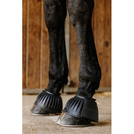 Horse wearing black protective boots on a wooden floor.