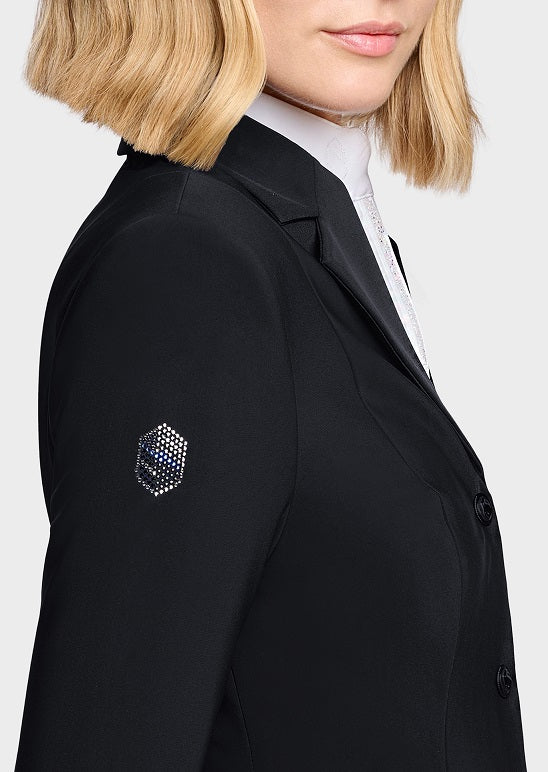 Close-up side view of a woman wearing a black blazer over a white collared shirt. The blazer has a small geometric embroidered patch on the upper sleeve.