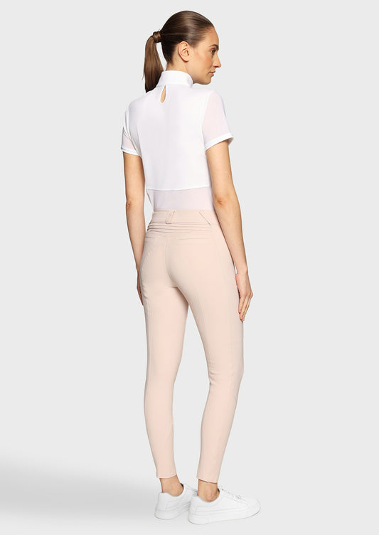 Woman wearing a white competition shirt and pink breeches on a beige background
