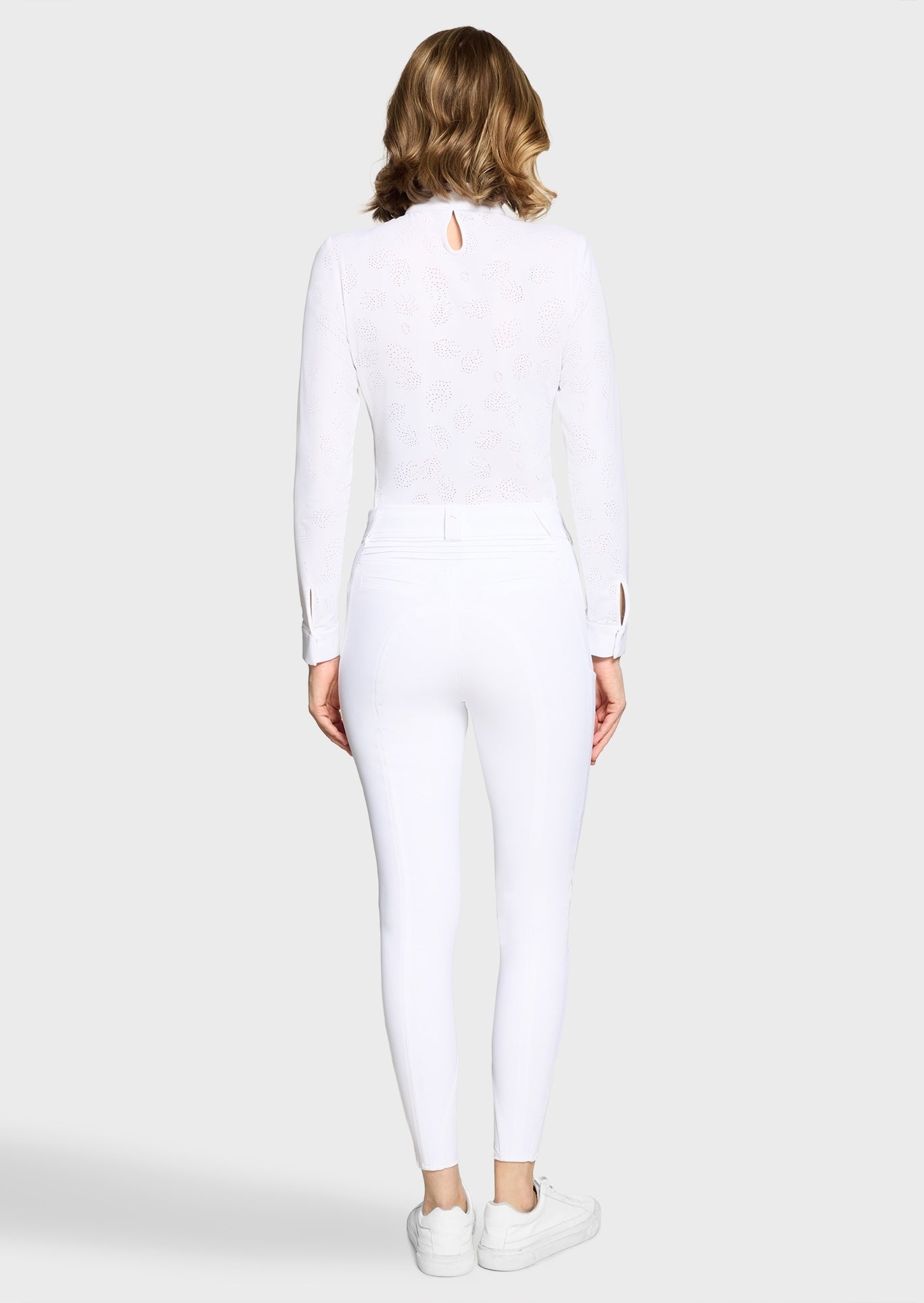 Woman wearing a white competition shirt and white breeches on a beige background