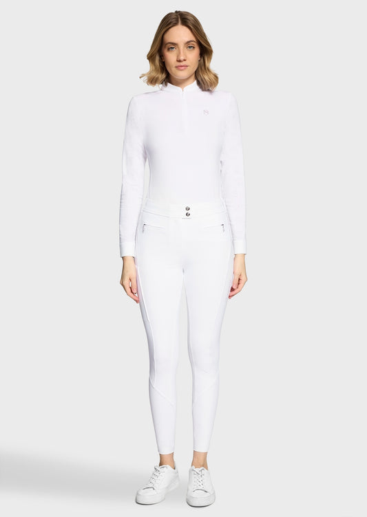 Woman wearing a white competition shirt and white breeches on a beige background