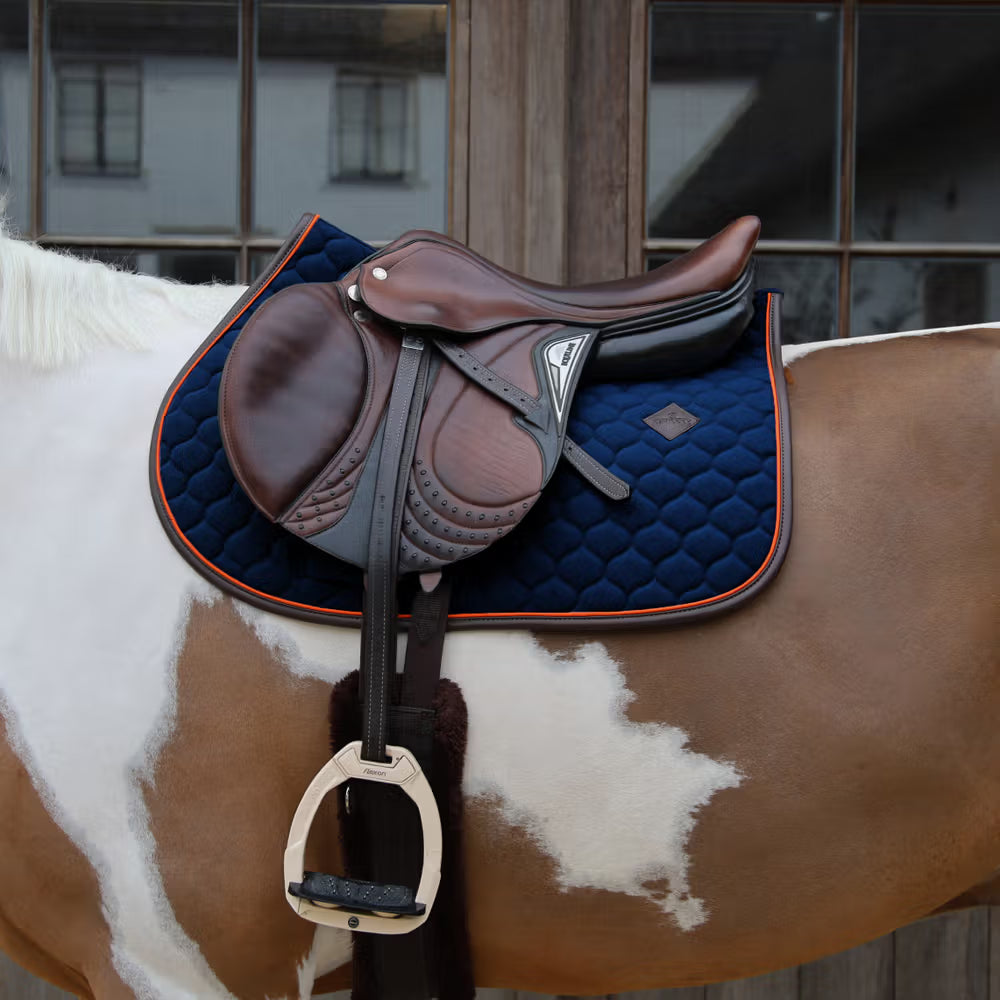 Brown saddle on a horse with a blue pad, against a blurred indoor background.
