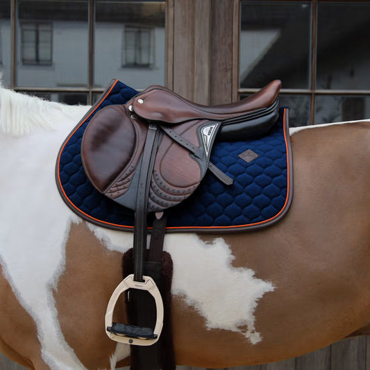 Brown saddle on a horse with a blue pad, against a blurred indoor background.