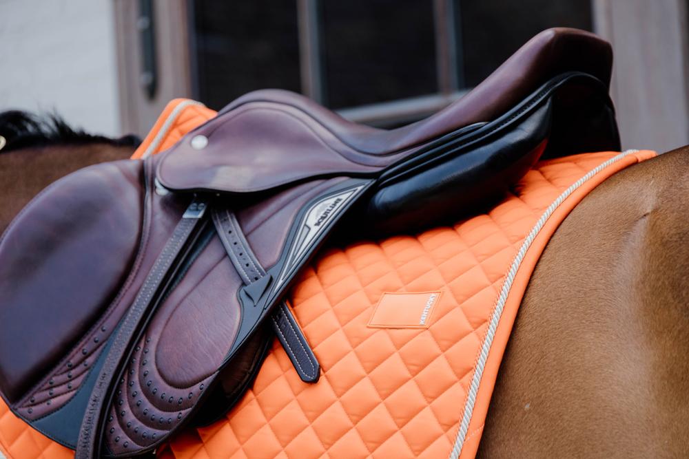 Saddle on an orange quilted pad on a horse