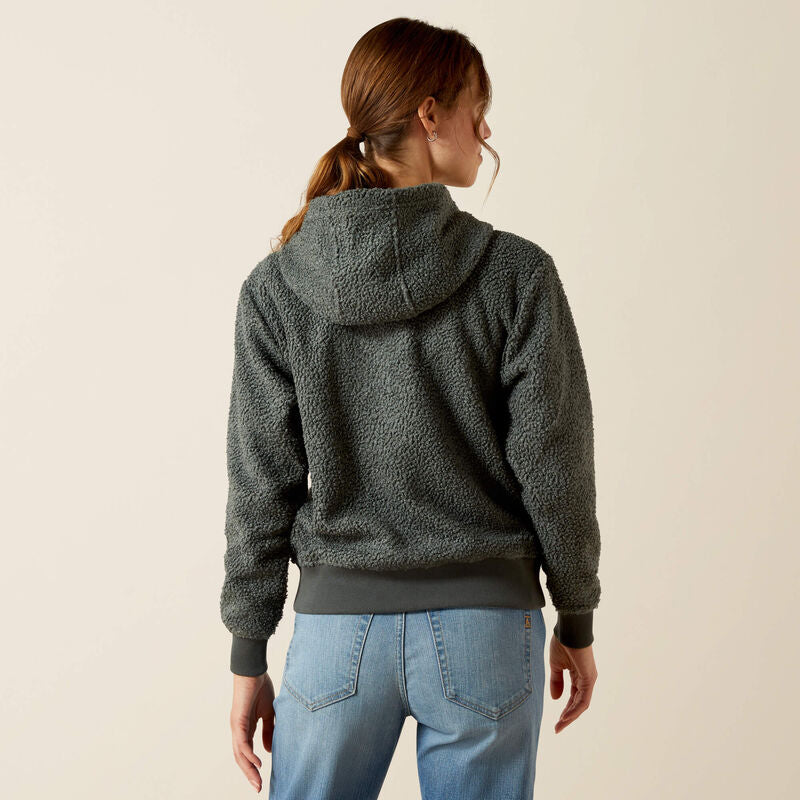 Person wearing a dark green fleece hoodie and blue jeans on a beige background