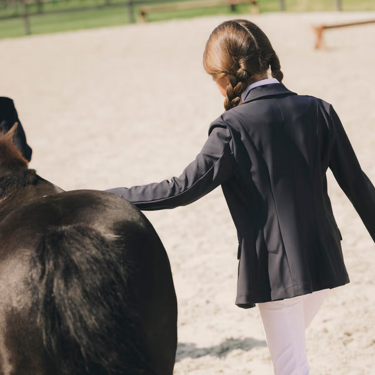 Person in equestrian attire petting a horse in an outdoor arena