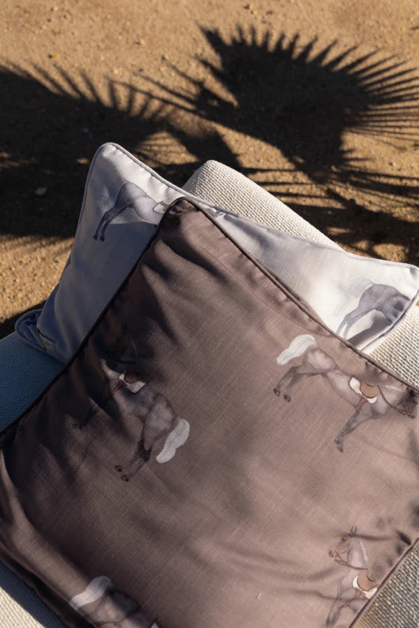 Close-up of a pillow on a sandy surface with palm leaf shadows.