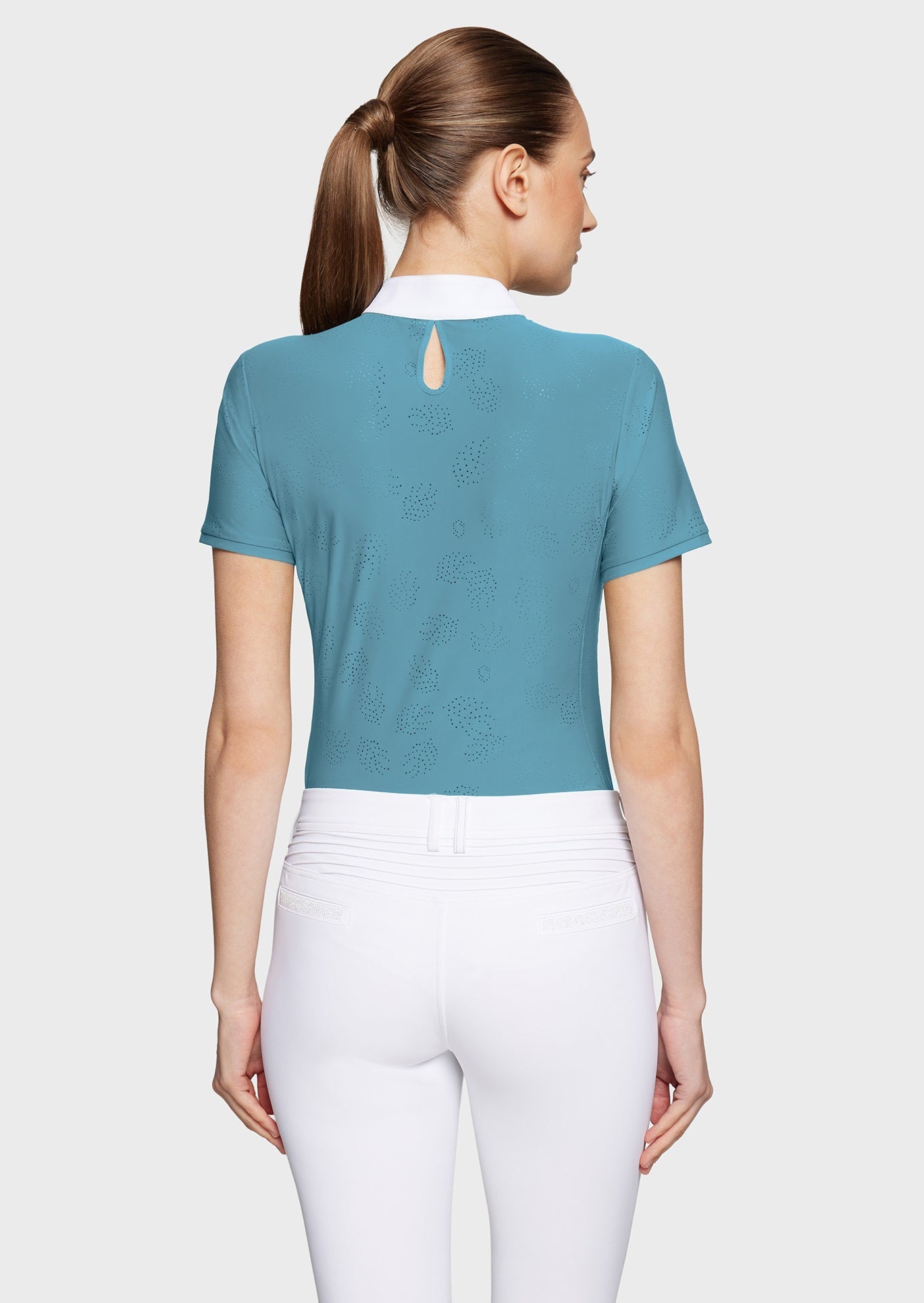 Woman wearing a blue competition shirt and white breeches on a beige background