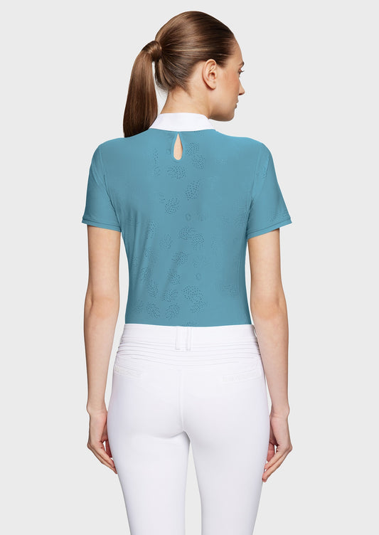 Woman wearing a blue competition shirt and white breeches on a beige background