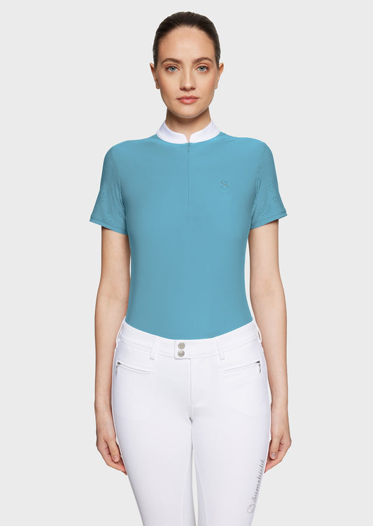 Woman wearing a blue competition shirt and white breeches on a beige background