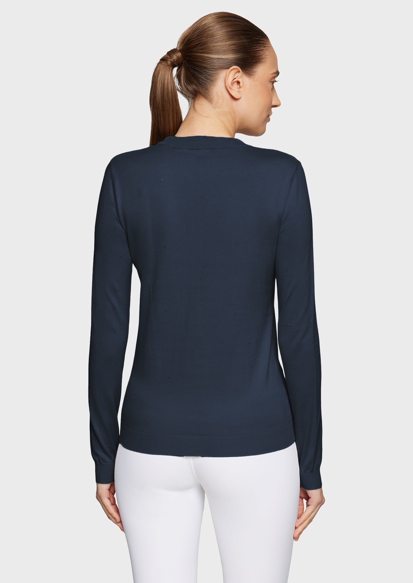 Woman wearing a navy pullover and white breeches on a beige background