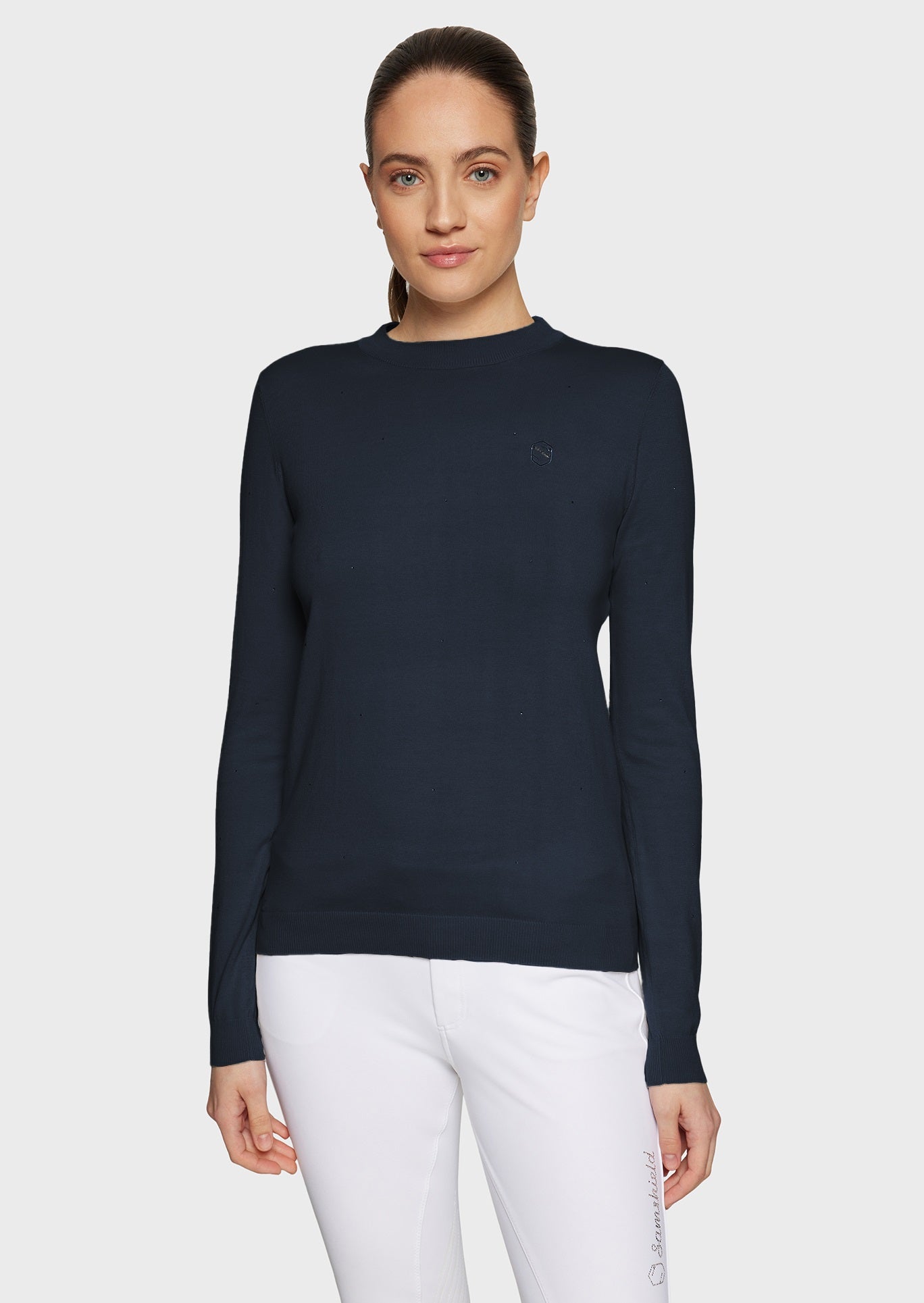 Woman wearing a navy pullover and white breeches on a beige background