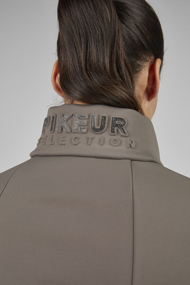 Person wearing a beige jacket with 'PIKEUR SELECTION' text on the collar against a gray background