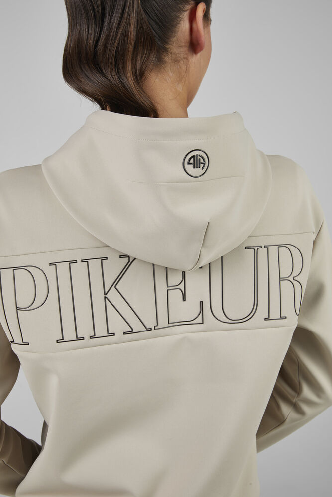 Beige hoodie with 'PIKEUR' branding on the back, worn by a person.