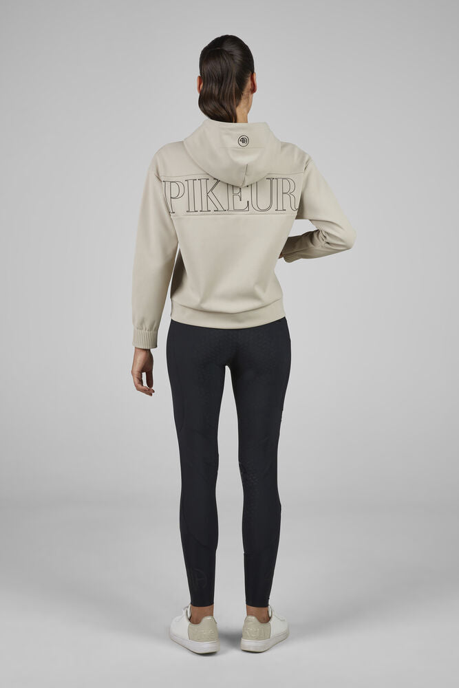 Person wearing a beige hoodie with 'PIKEUR' branding and black leggings on a gray background