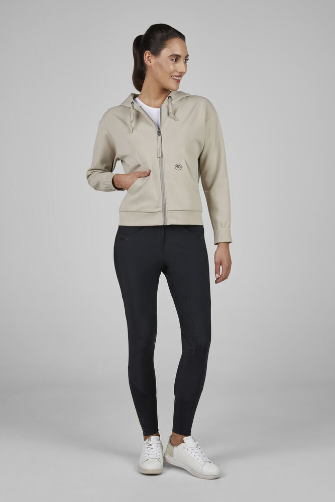 Woman wearing a beige jacket, black leggings, and white sneakers on a gray background