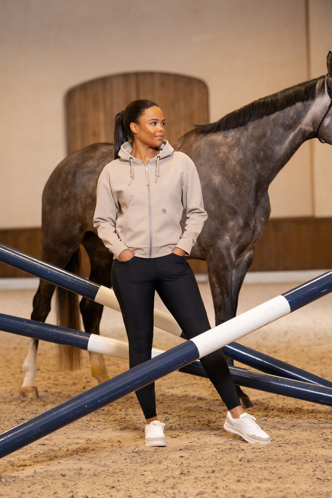 Woman standing next to a horse in an indoor arena with equestrian equipment.