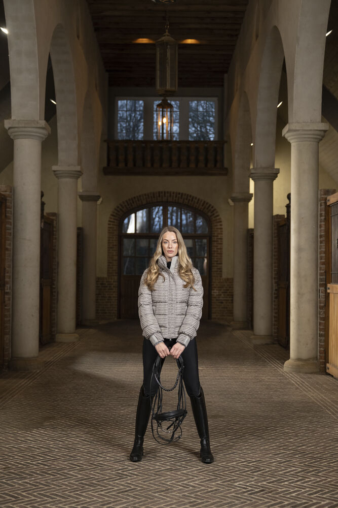 Woman holding skates in a large, open hall with high ceilings and arches.