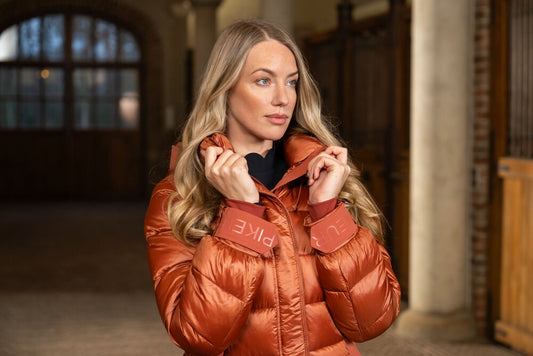 Woman wearing a brown puffer jacket with 'PIKEUR' branding in an indoor setting.