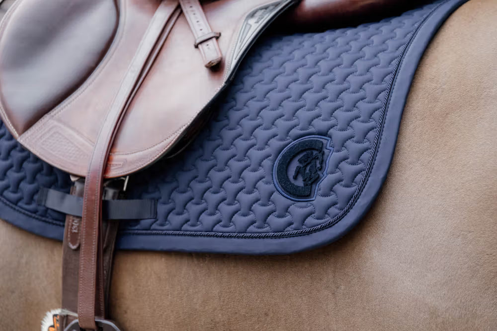 Close-up of a blue saddle pad on a horse with a brand logo.