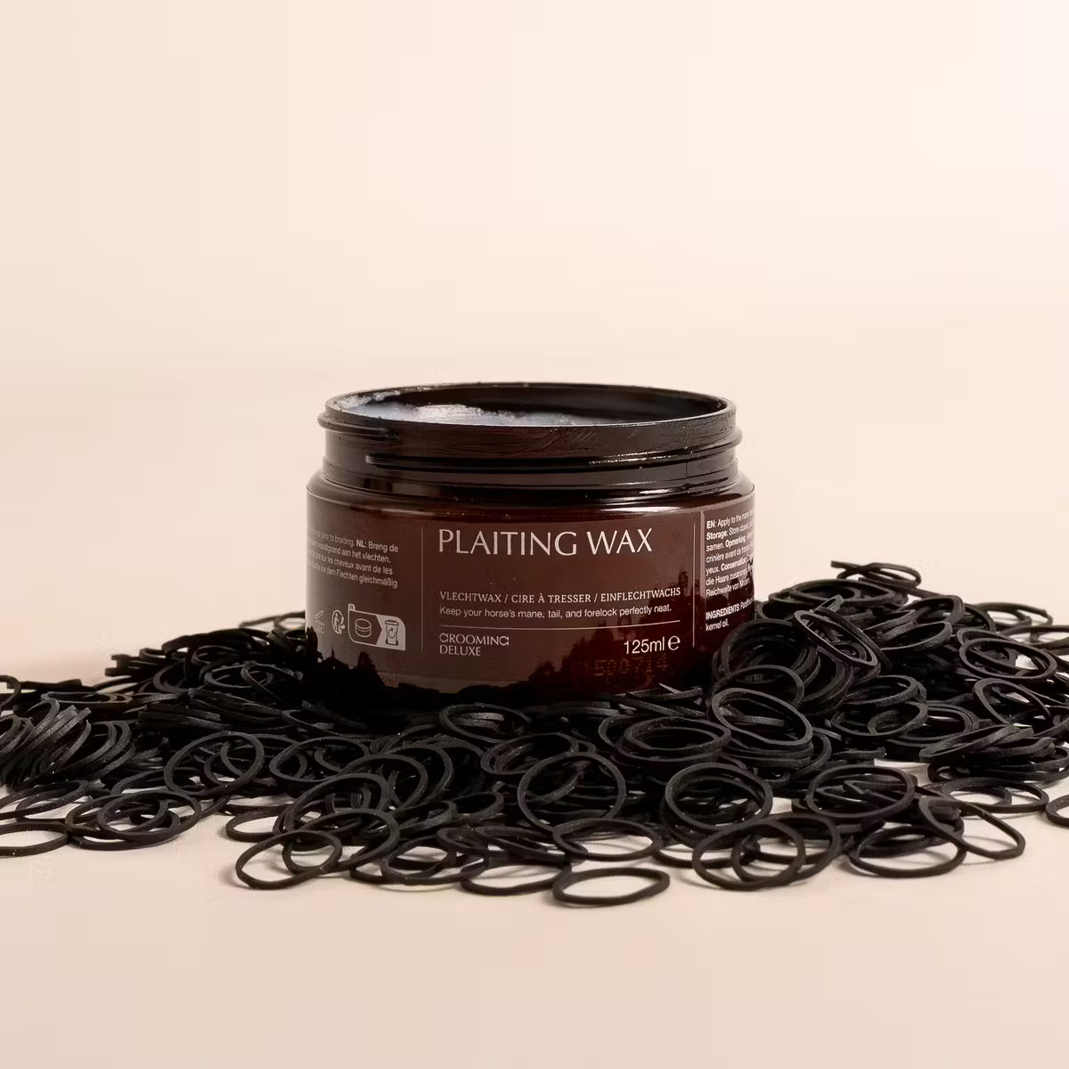 Jar of plaiting wax surrounded by black hair ties on a beige background