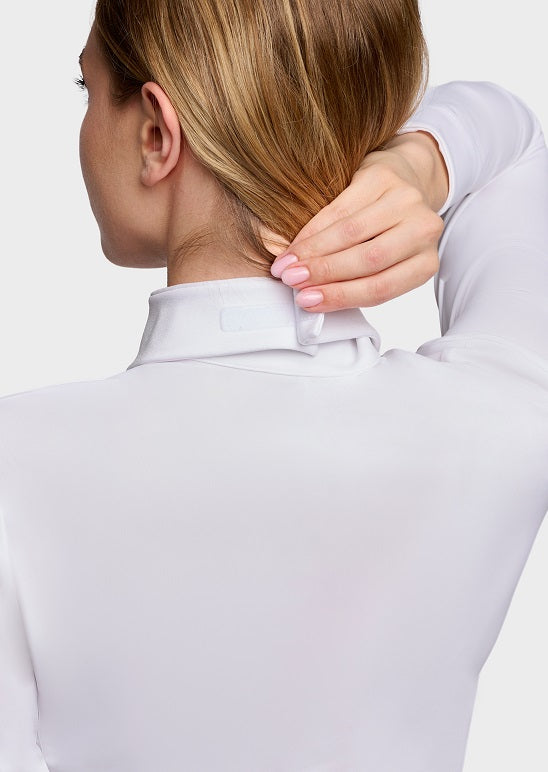 Close-up back view of a woman wearing a white long-sleeve high-neck top, adjusting the collar with her hand against a light gray studio background.