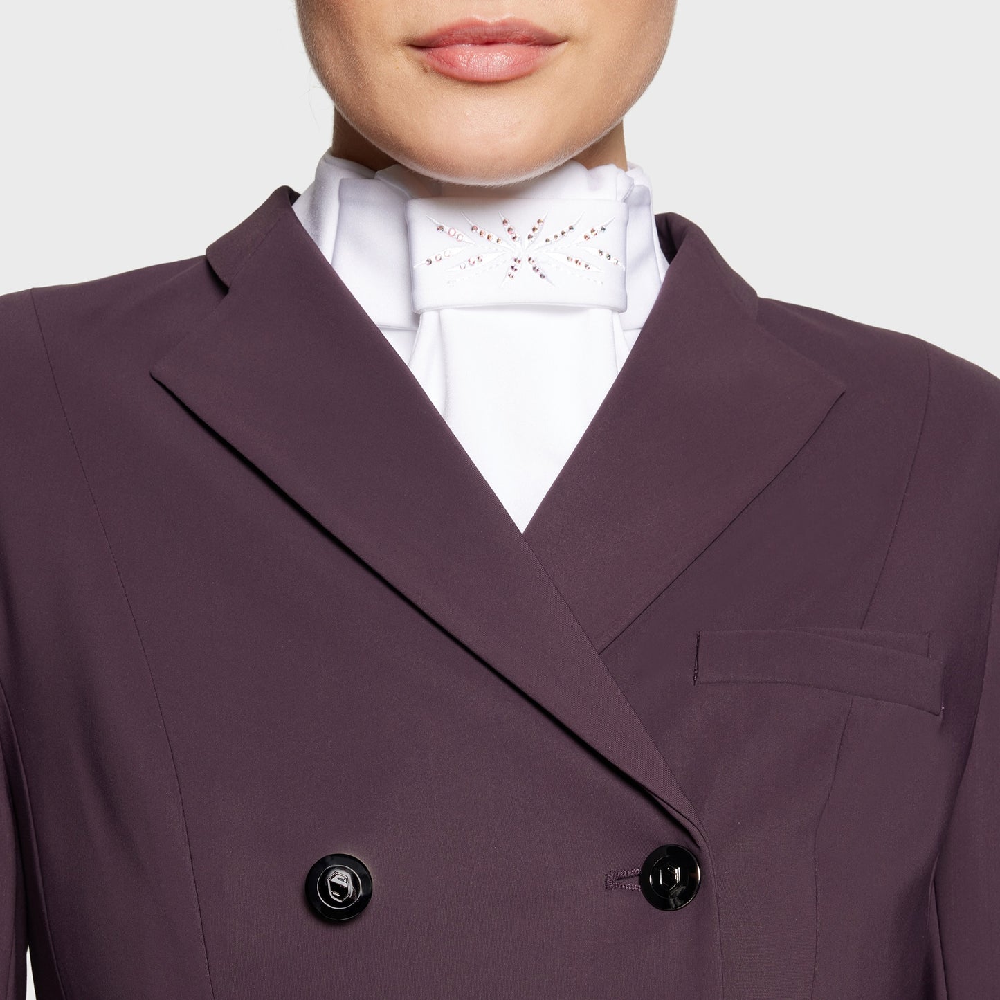 Close-up of a person wearing a purple blazer over a white shirt with a white dressage stock.