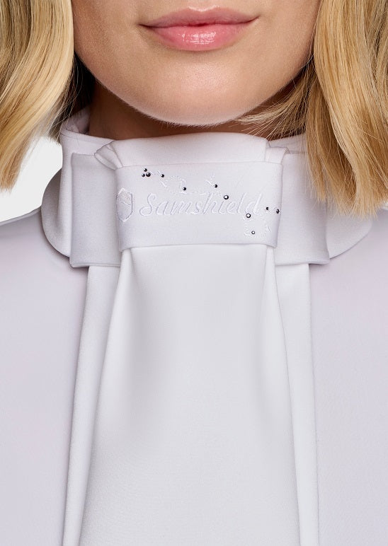 Close-up of a model wearing a white high-neck bow collar blouse with rhinestone embellishments and the brand name 'Samshield' embroidered on the front.
