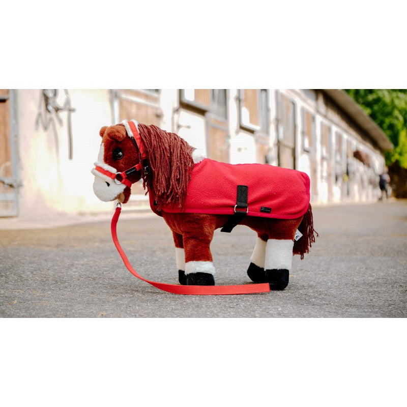 Plush horse toy with a red blanket and white bridle on a leash, standing on a street.