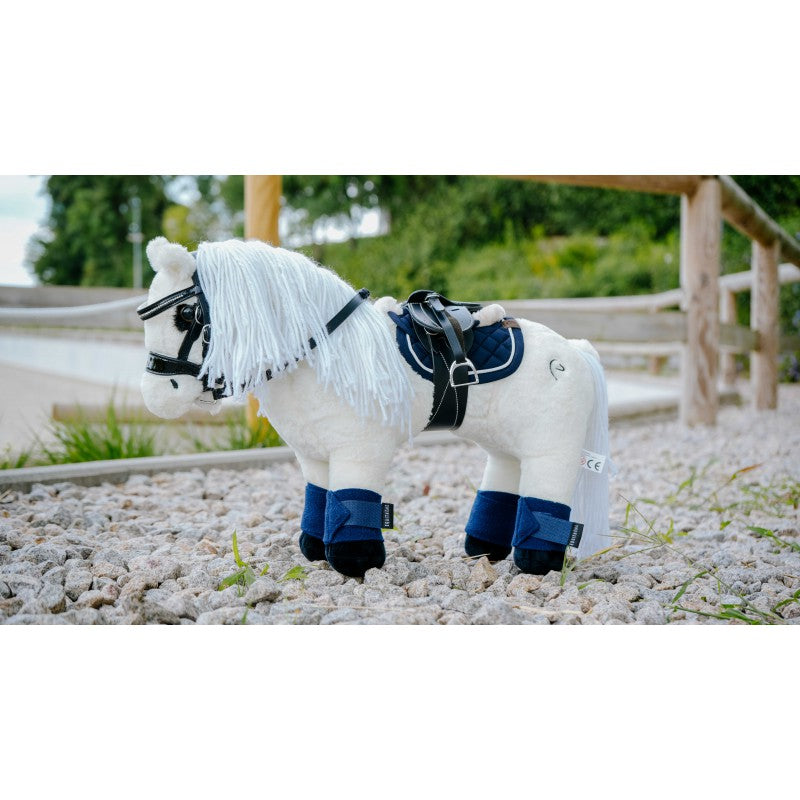 White toy horse with blue legs and black bridle on a gravel surface with greenery in the background