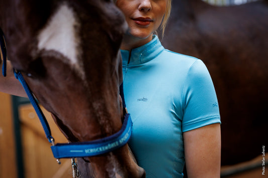 Woman in a blue equestrian shirt standing next to a horse